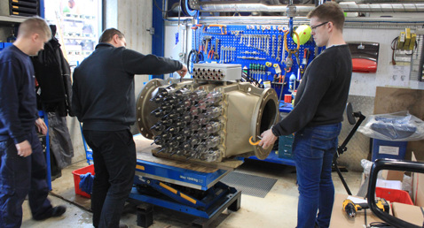 Three technicians work on large industrial equipment in a workshop.