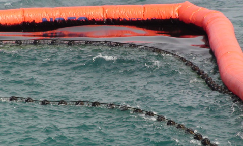 Orange oil containment boom floating on the ocean surface, capturing oil spill.