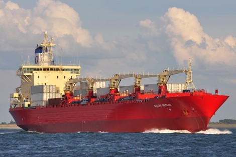 Red cargo ship sailing on the ocean under a partly cloudy sky.