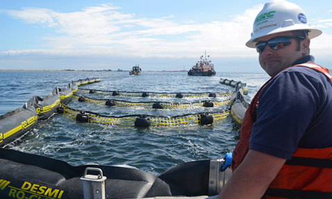 Man observing DESMI RO-CLEAN oil containment boom at sea.