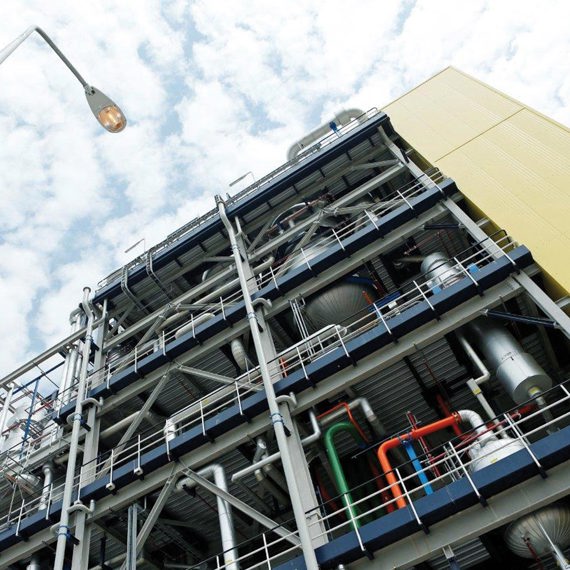 Industrial building with complex piping system and streetlamp under a cloudy sky.