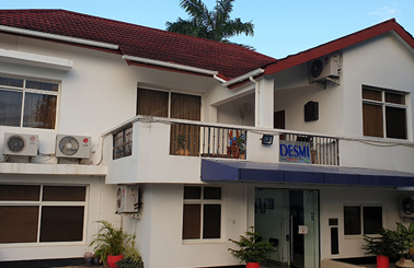 White building with "DESMI" signage, featuring air conditioning units and plants.