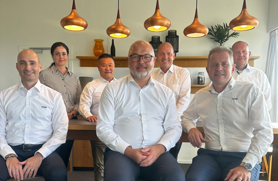 Group of six professionals posing in a modern office setting.