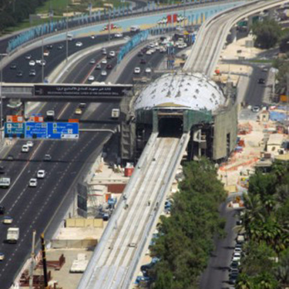 Elevated train line under construction above busy city highway, surrounded by buildings.