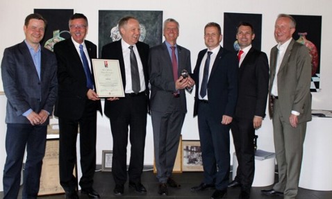 七位身穿西装的男士微笑，其中一人手持证书，另一人手持奖杯。