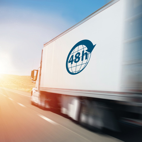 Lastbil med "48h"-logo kører hurtigt ned ad en motorvej ved solopgang.