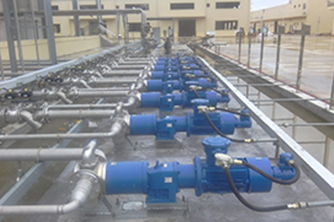 Blue industrial pumps in a line, connected to metal piping for fluid handling.