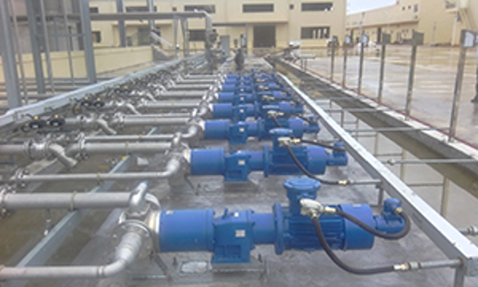 Blue industrial pumps in a line, connected to metal piping for fluid handling.