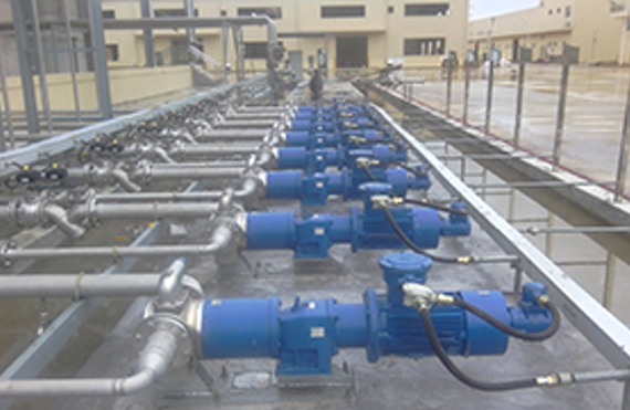 Blue industrial pumps in a line, connected to metal piping for fluid handling.