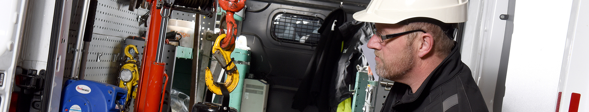 Worker in hard hat operates equipment inside a vehicle, handling tools and machinery.