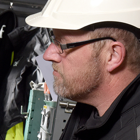 Worker in hard hat operates equipment inside a vehicle, handling tools and machinery.