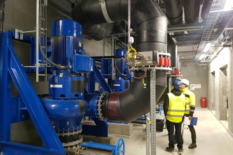 Workers inspecting large industrial pumps and pipes in a facility.