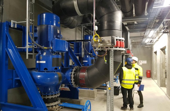 Workers inspecting large industrial pumps and pipes in a facility.