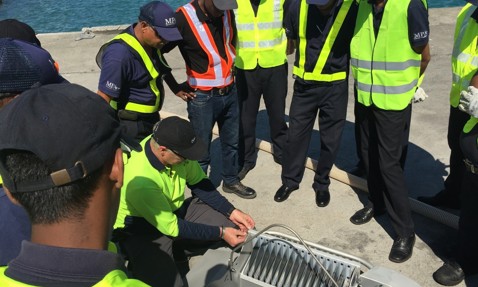 身穿安全背心的工人们聚集在水边的设备周围。