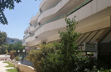 Modern building with balconies surrounded by greenery on a sunny day.