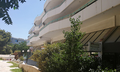 Modern building with balconies surrounded by greenery on a sunny day.
