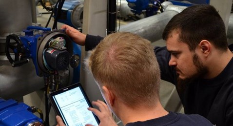 Two technicians using a tablet to inspect industrial equipment in a facility.