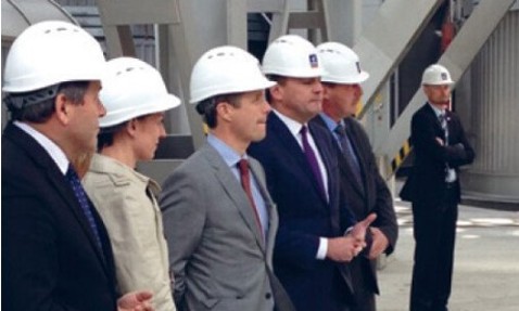 People in suits and white helmets standing at an industrial site.