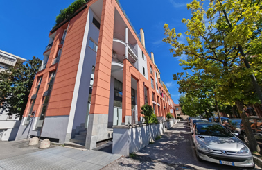 Modern orange building with large windows, cars parked nearby, and trees lining the street.