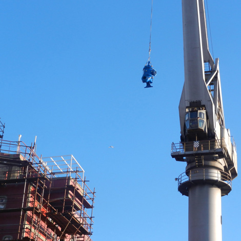 Crane lifting a blue pump beside a construction site against clear blue sky.