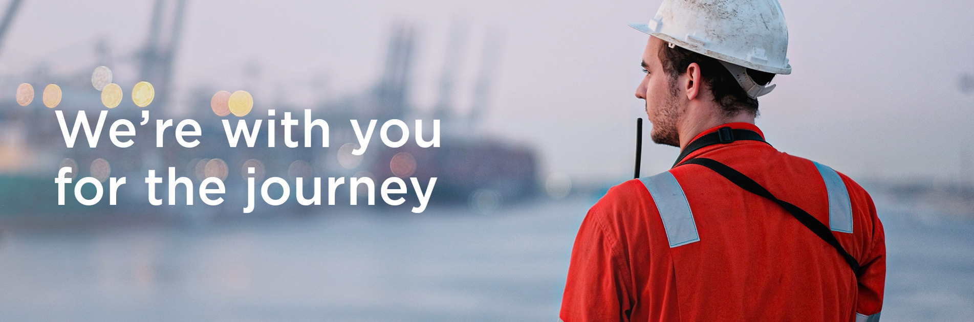 Worker in safety gear observing harbor, with text: "We're with you for the journey."