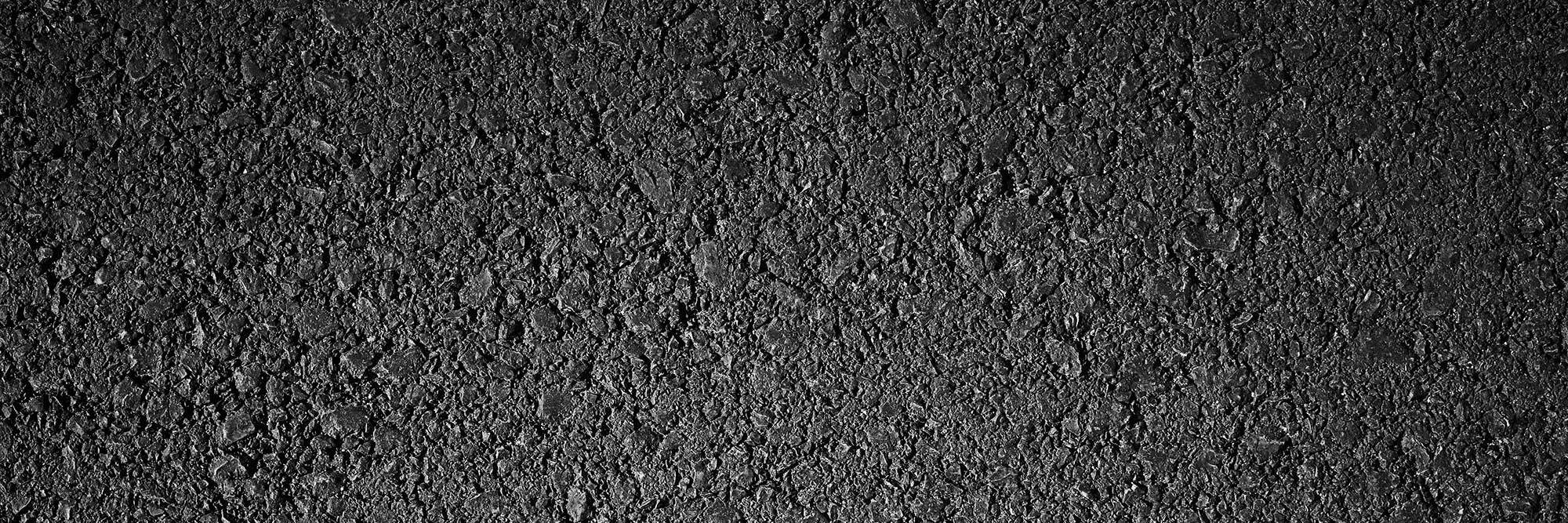 Close-up of rough black asphalt texture with visible granules and stones.
