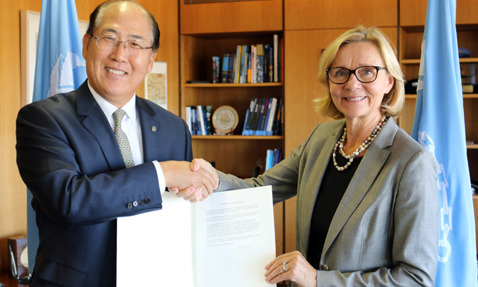 Two individuals handshake and hold a document in an office setting.