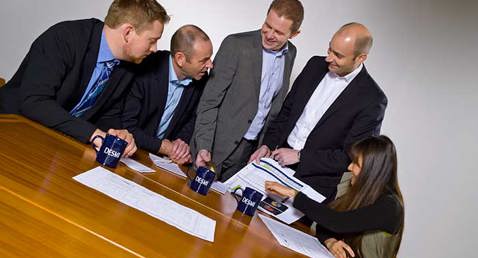 Group discussing documents at a table with DESMI mugs visible.