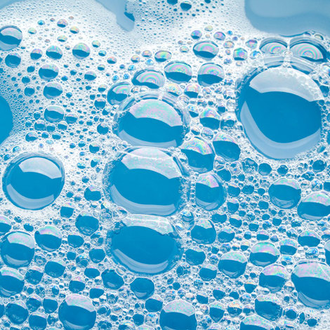 Close-up of soap bubbles on a blue liquid surface.