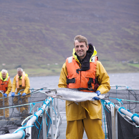 Man in orange life jacket holding large fish on aquaculture farm.