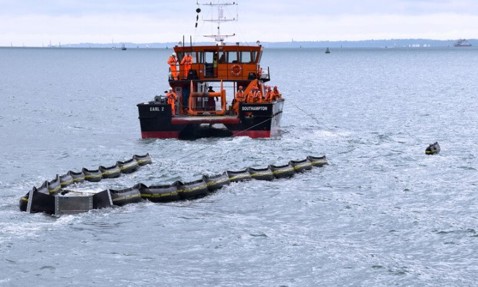 Boat towing an oil containment boom in open water for environmental protection.