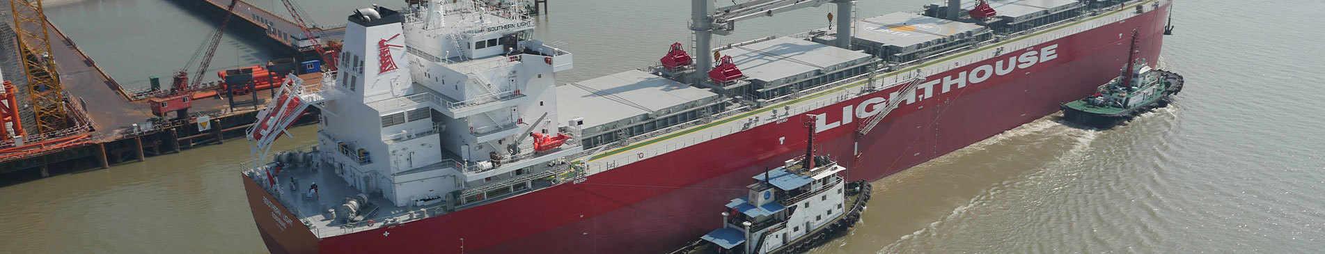 Large red ship named "Lighthouse" assisted by two tugboats in a harbor.