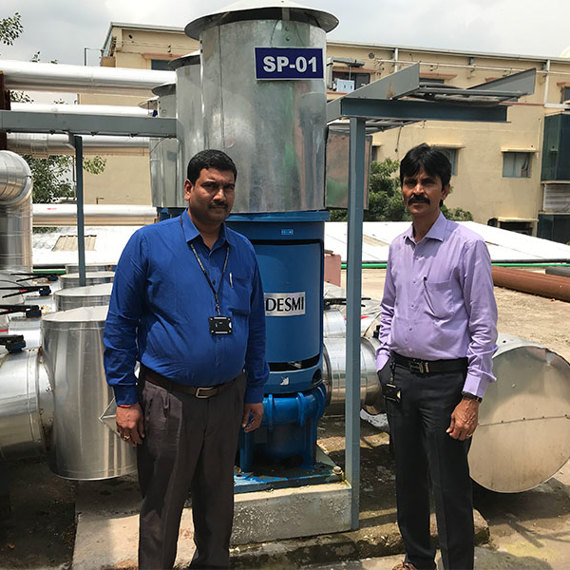 Two men standing beside a DESMI pump for fluid handling in an industrial setting.