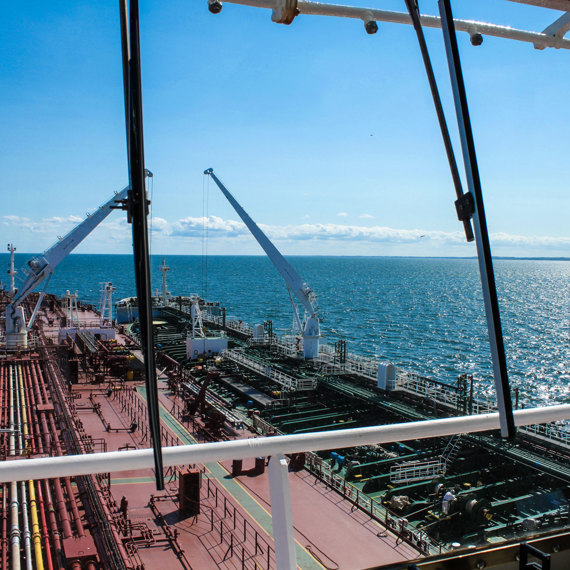 View from ship's bridge overlooking deck and ocean under clear blue sky.