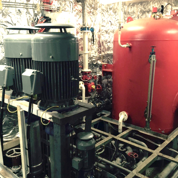 Industrial room with large pumps and a red pressure vessel for fluid handling.