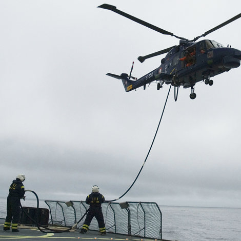 Helicopter refueling operation on a ship, two crew members handling hose.