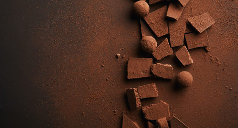 Cocoa-dusted chocolate pieces and truffles scattered on a dark surface.