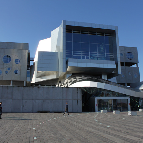 Modern architectural building with geometric design and people walking in the foreground.