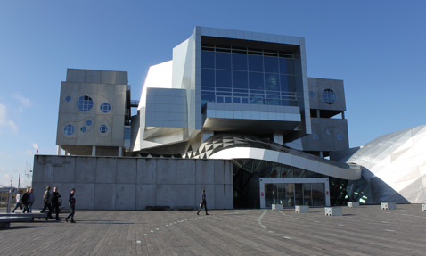 Modern architectural building with geometric design and people walking in the foreground.