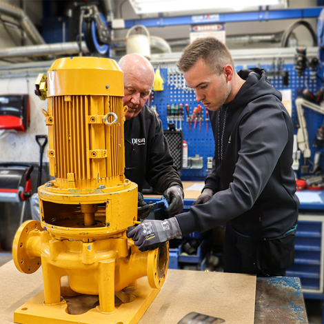 Two technicians working on a DESMI pump in a workshop.