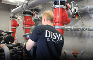 Technician in DESMI Service shirt working with industrial piping system.