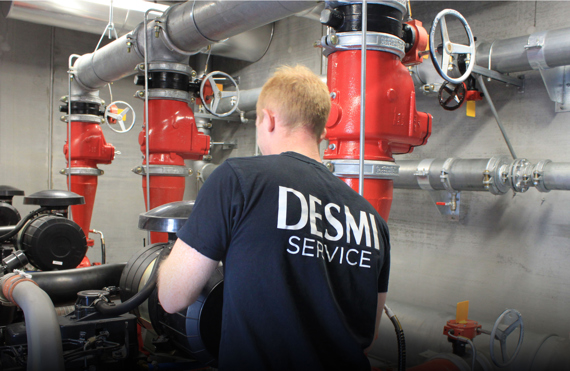 身穿DESMI服务衬衫的技术人员正在处理工业管道系统。