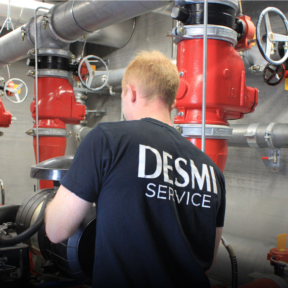 Technician in DESMI Service shirt working with industrial piping system.