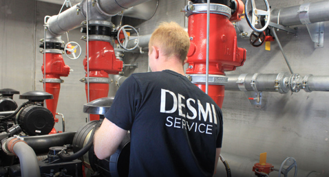 Techniker im DESMI Service-Hemd arbeitet mit einem industriellen Rohrleitungssystem.