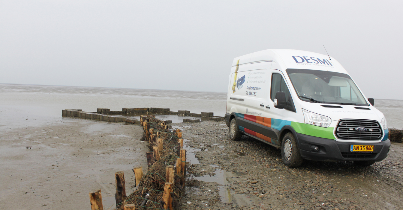 DESMI service van parked on a rocky shoreline near the water.