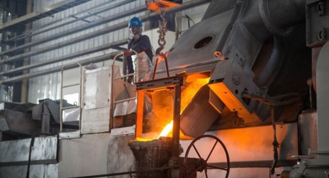 Worker overseeing molten metal being poured in an industrial foundry setting.