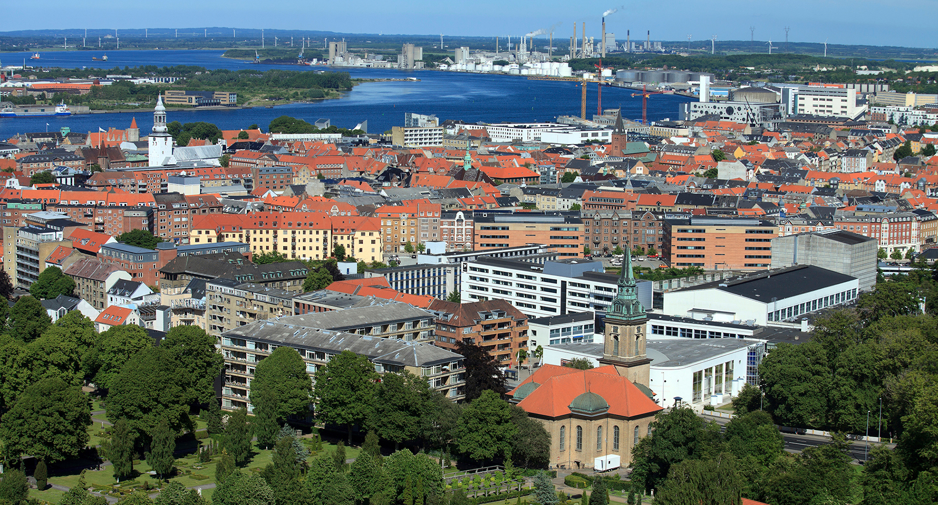 Flygfoto av en kuststad med röd-takade byggnader och industriell bakgrund.