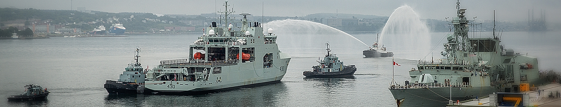 海港中的海军舰艇和拖船，背景有水柱喷射。