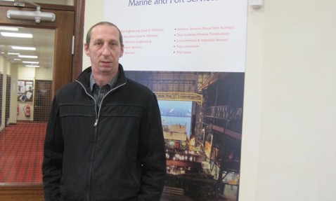 Man standing in front of marine and port services poster indoors.