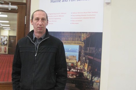 Man standing in front of marine and port services poster indoors.